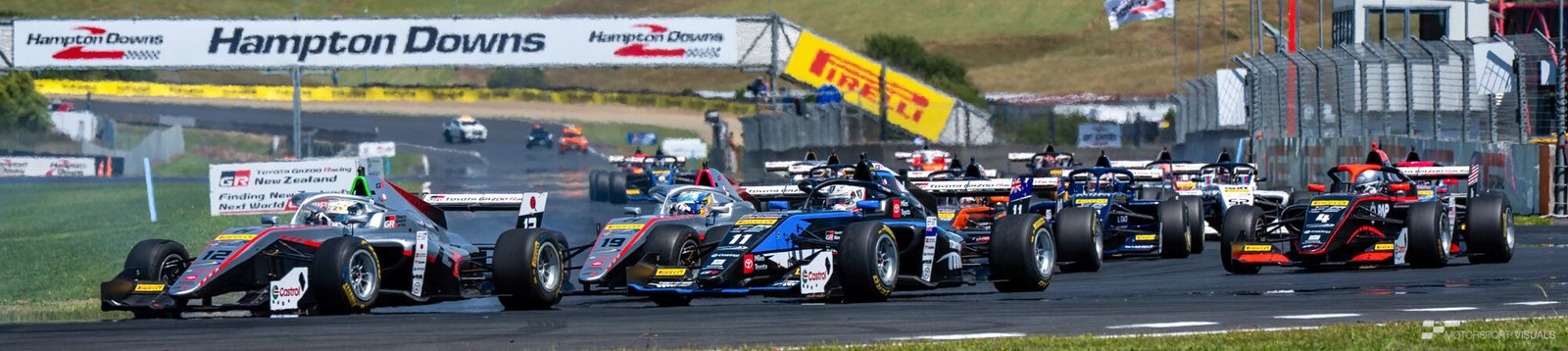 A race scene at Hampton Downs featuring several Formula 1-style race cars lined up on the track during a sunny day.